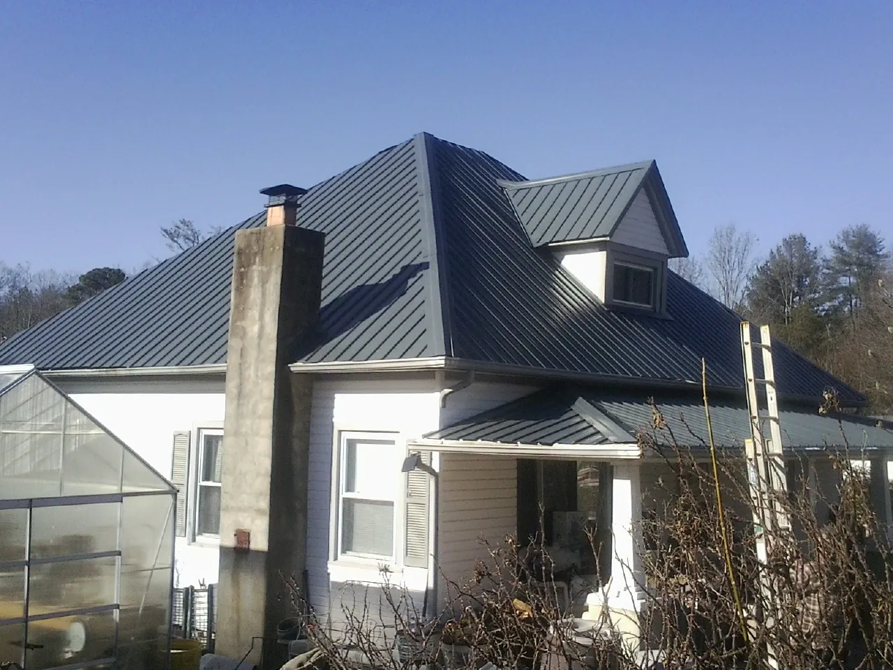 Dark blue standing seam metal roof on a white farmhouse with dormer — Slate & Tile Roof Repair by Roofing Brothers in Tigrett