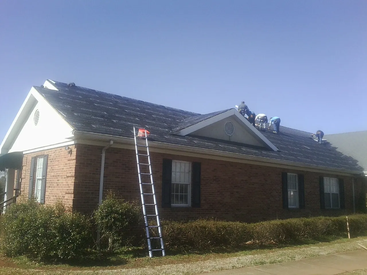 Crew tearing shingles off a brick ranch roof with a ladder set — Emergency Roof Repair work by our crew in Tigrett