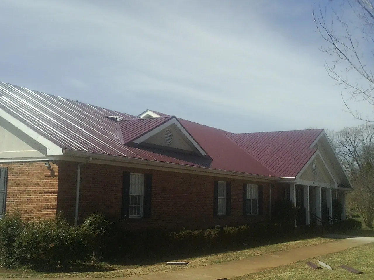 Red metal roof with gabled entries on a long brick building, from a Hail Damage Roof Repair job in Tigrett