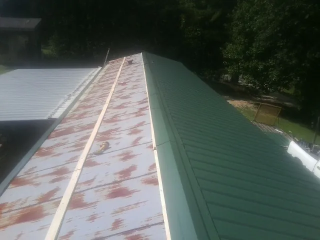 Old rusted panels beside newly installed green metal roofing — Wind Damage Roof Repair by Roofing Brothers in Tigrett