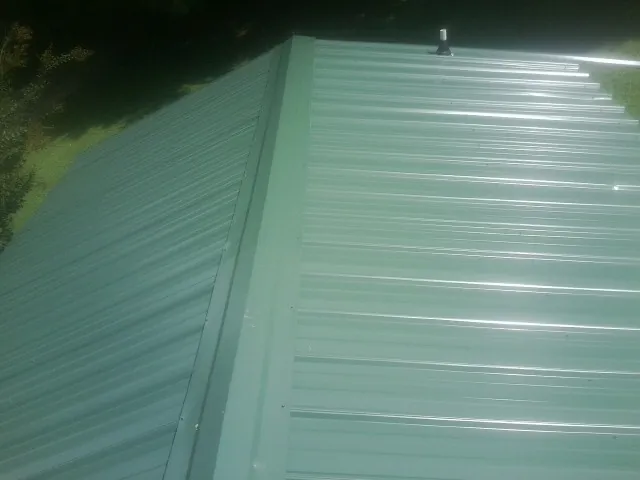 New green metal panels meeting at the ridge of a roof — Flat Roof Repair work by our crew in Tigrett