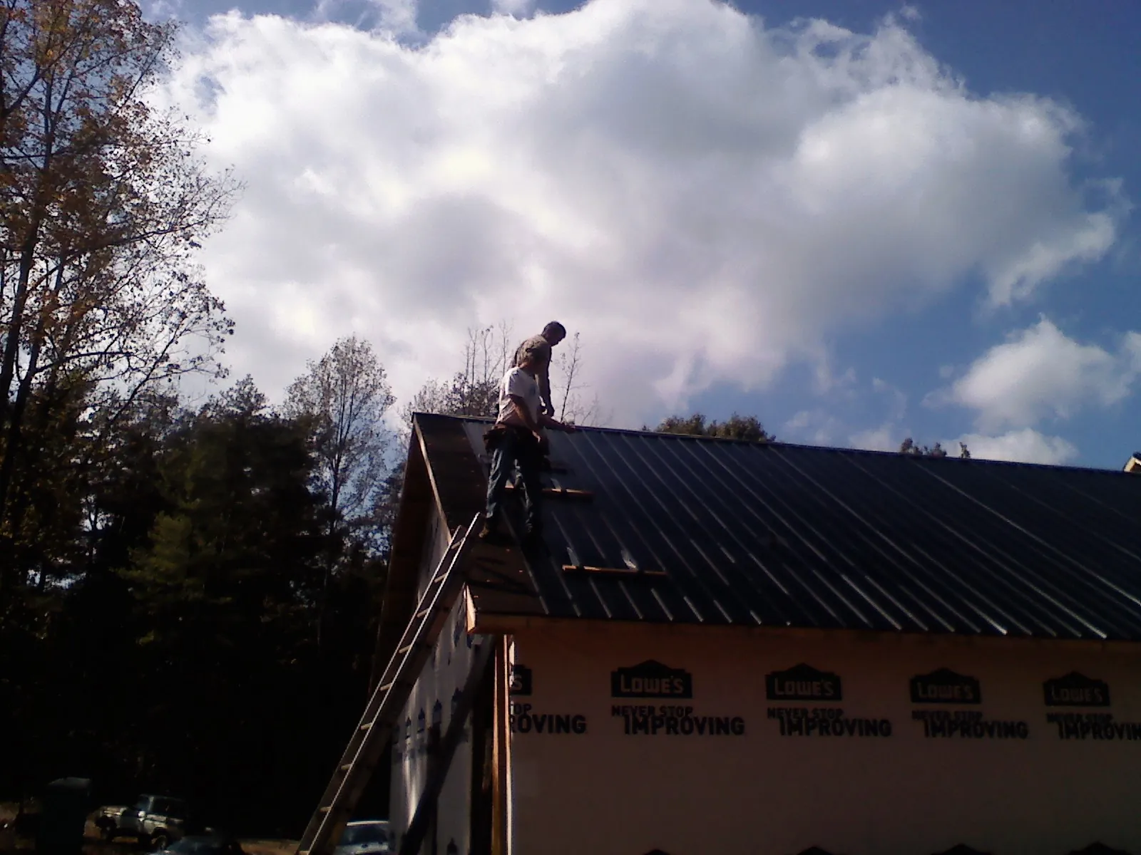 Roofer fastening dark metal panels high against a cloudy sky, from a Roof Inspection job in Tigrett