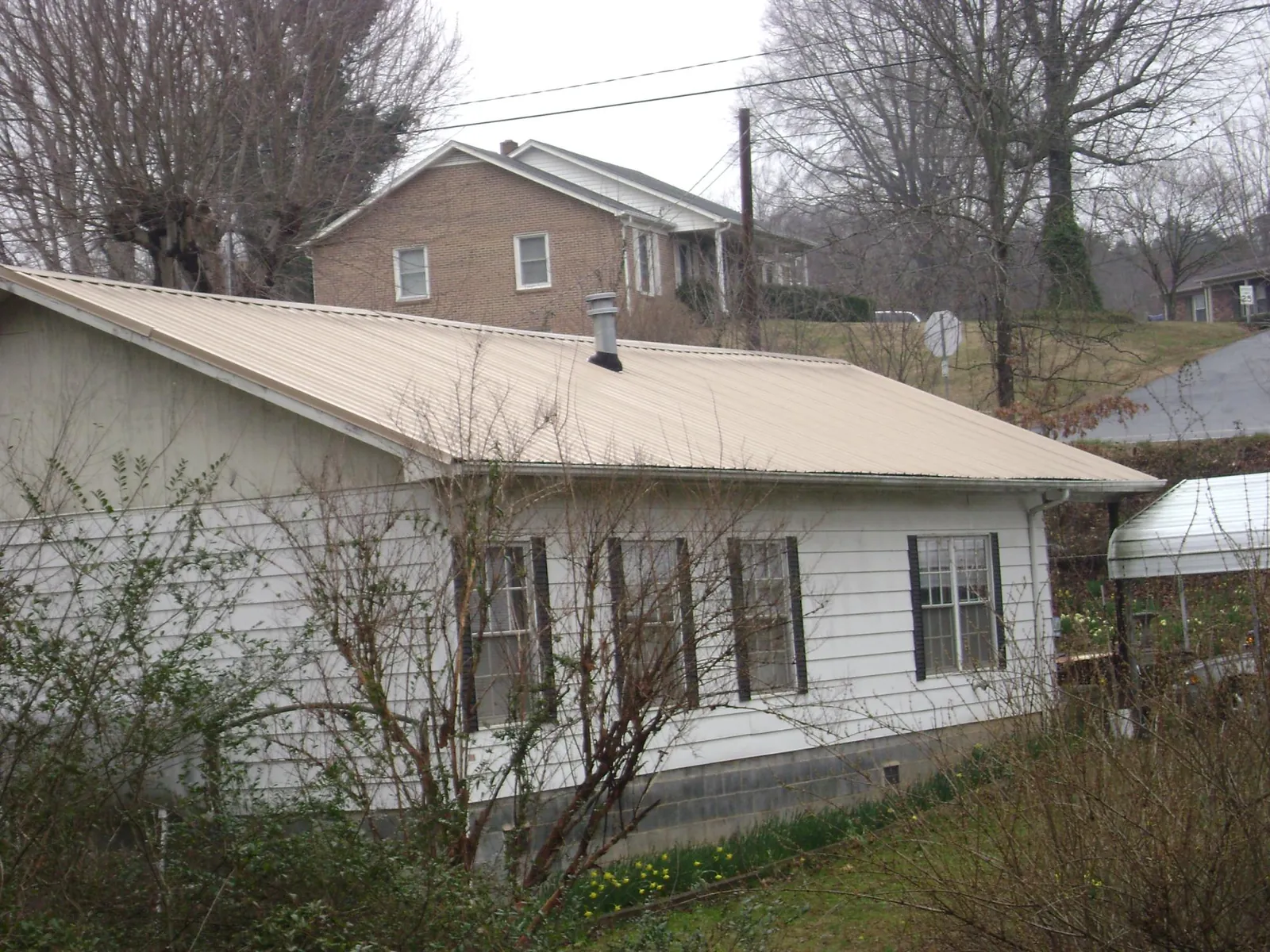 Tan metal roof on a white sided house set into a hillside — Commercial Roofing by Roofing Brothers in Tigrett
